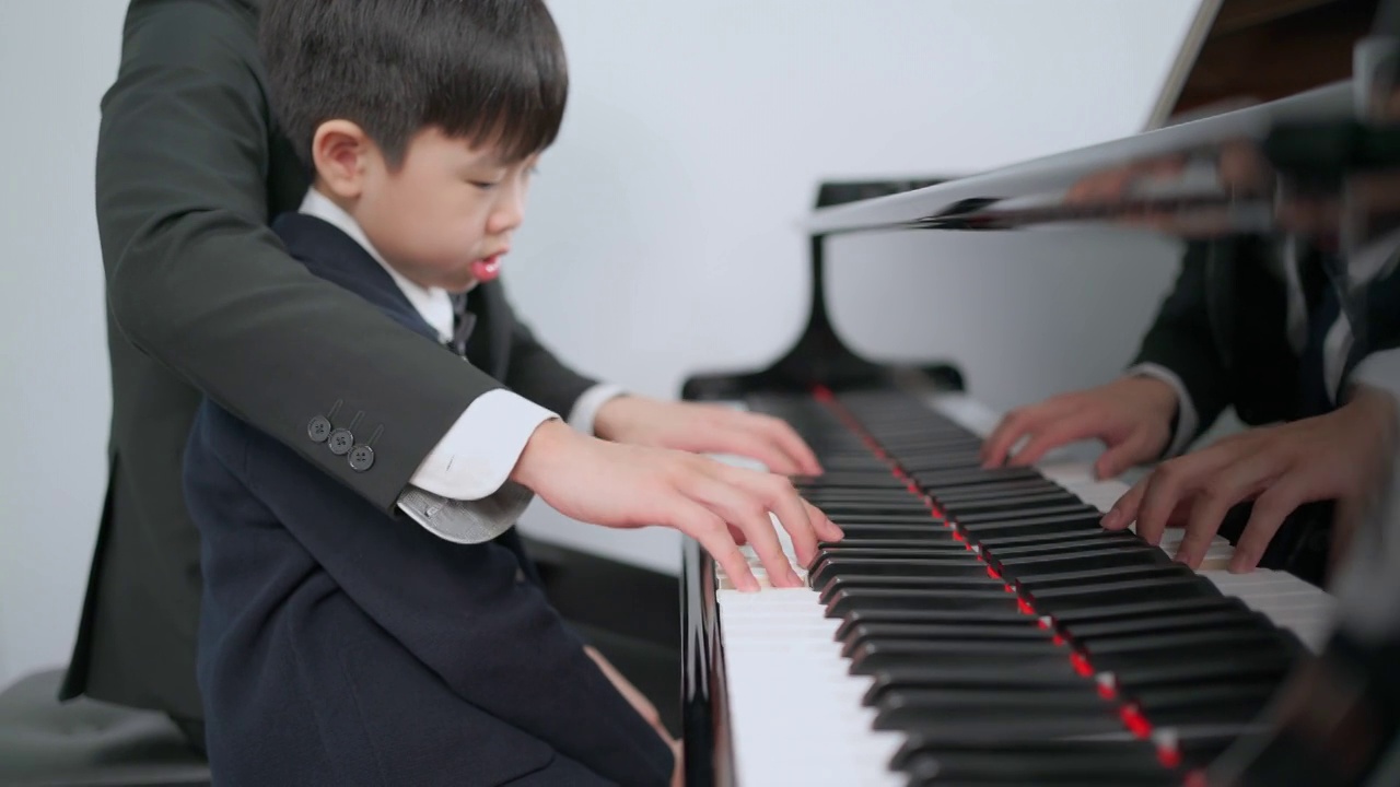 钢琴家在学校的教室里教一个男孩弹钢琴。最喜欢的古典音乐。在学习中快乐和乐趣。身着正式优雅套装的音乐家。教育、练习、放松的理念。视频素材