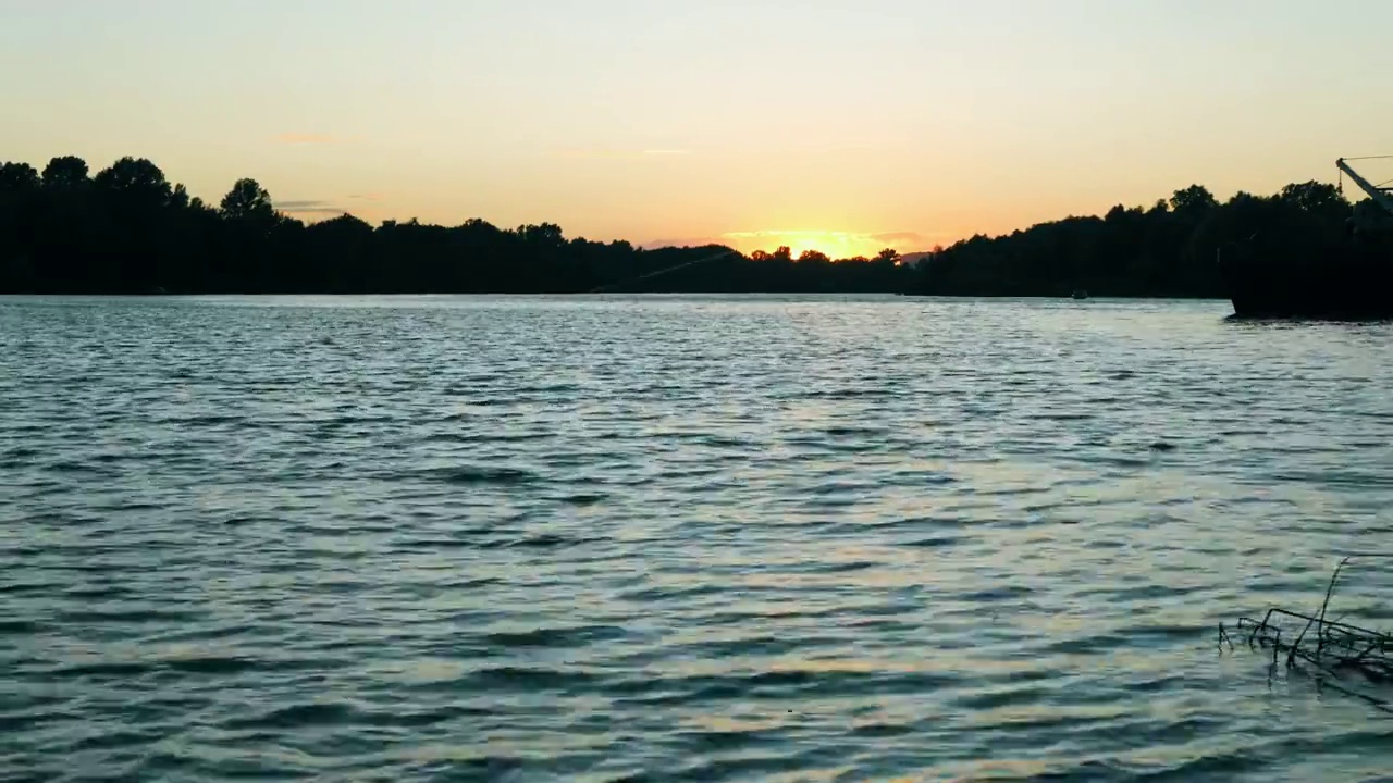 在落日的余晖中，河流的波浪和森林的美丽景色。愉快的夜晚的风景。船在大海背景下的剪影鱼竿线在风中摇摆视频素材