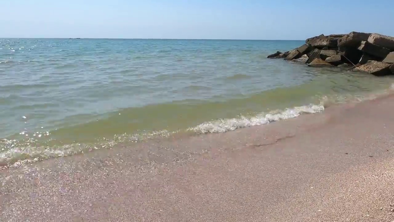 白浪穿过海面上岩石的缝隙，拍打在沙滩上。荒野海滩上的岩石碎片视频素材