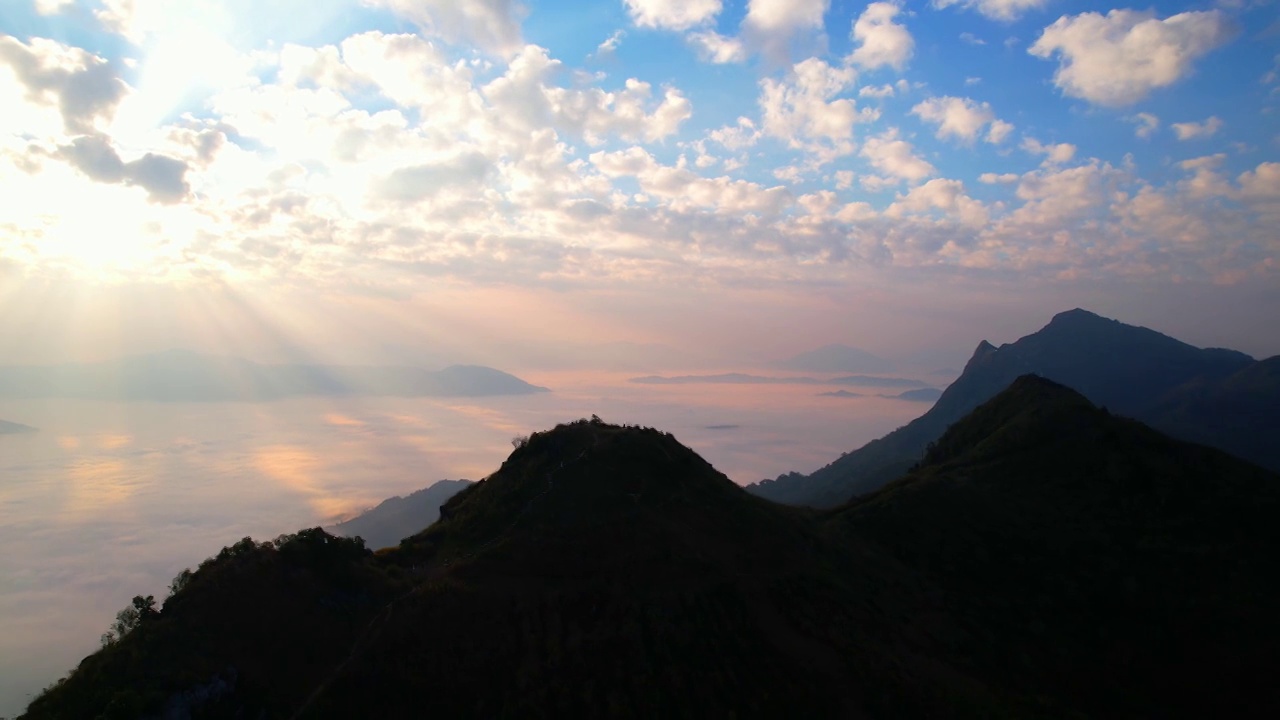 早晨，太阳的光线穿过云层，照射到山上雾蒙蒙的海面上。日出时拍摄4K航拍视频素材