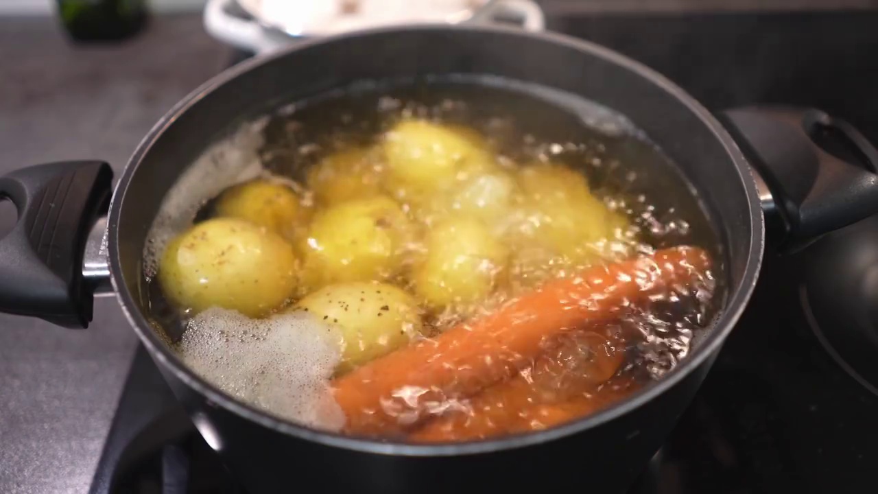 土豆和胡萝卜在沸水中的慢动作视频。用平底锅煮生蔬菜视频素材