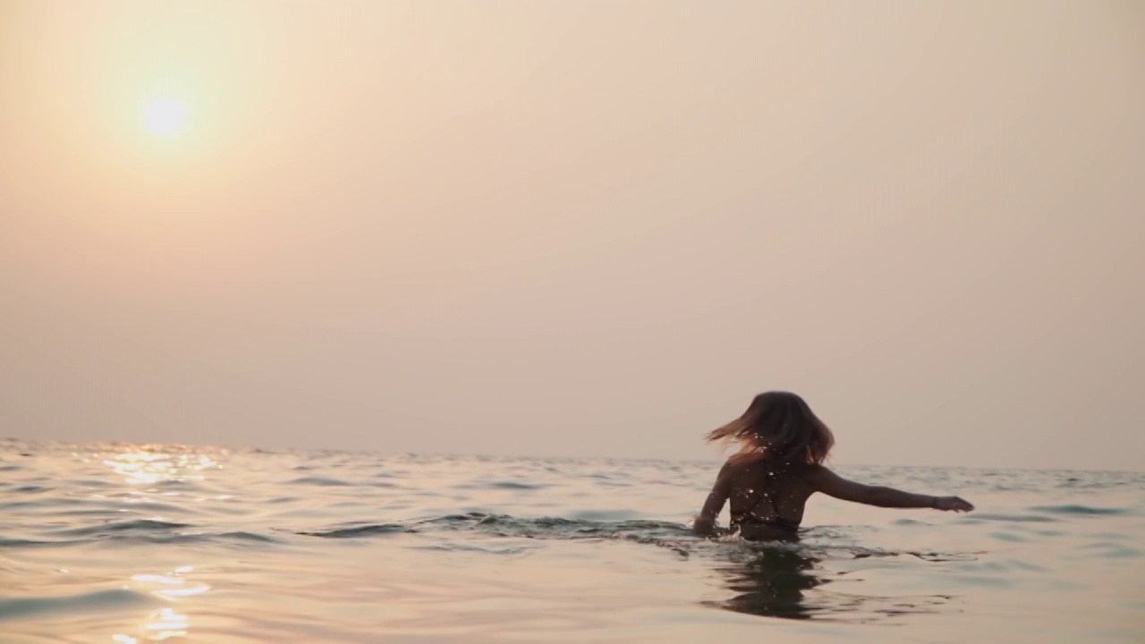 女孩在夕阳的映衬下在海里洗澡视频下载