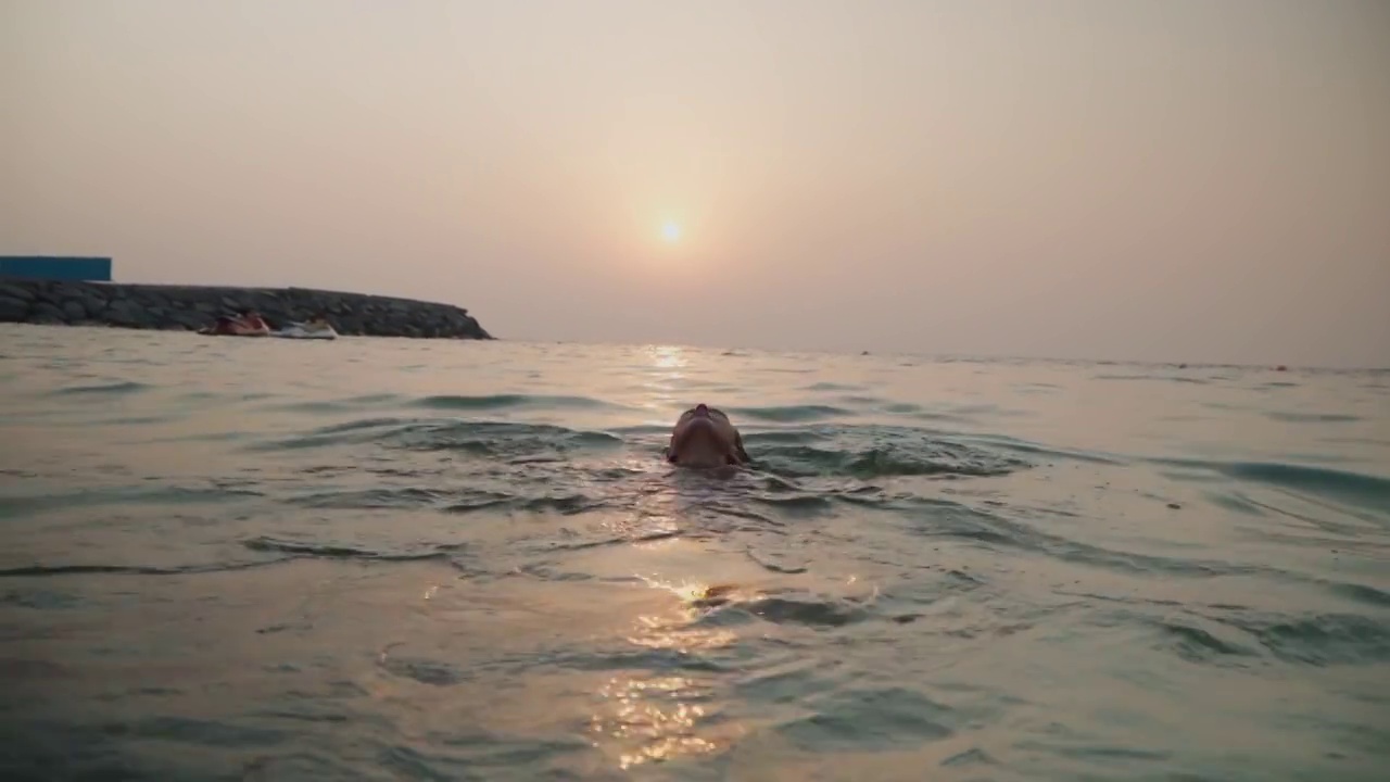 女孩在夕阳的映衬下在海里洗澡视频素材