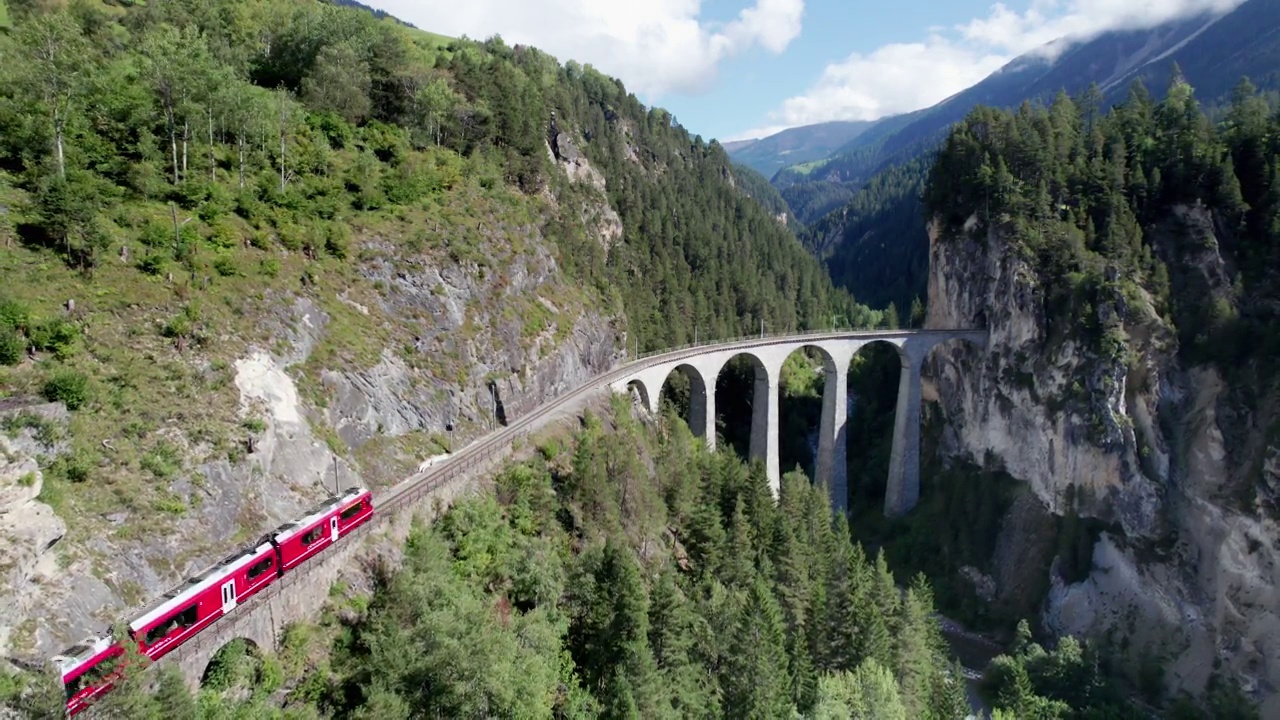 一列红色列车在瑞士阿尔卑斯山的Landwasser高架桥上行驶的鸟瞰图视频素材