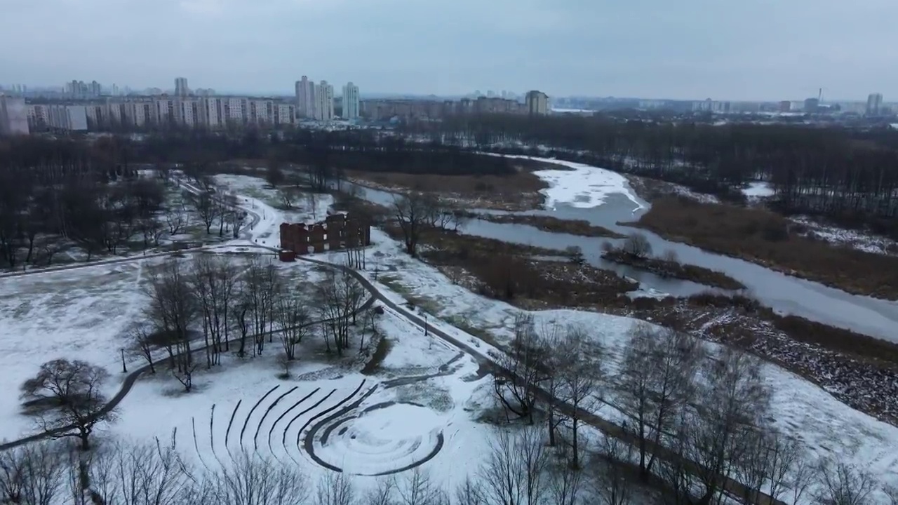 在白雪覆盖的城市公园上空飞行。可以看到由石头组成的圆形剧场和一条河。航空摄影。视频素材