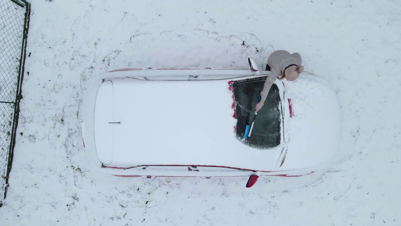 鸟瞰图，一个女人在清理她车上的雪视频素材