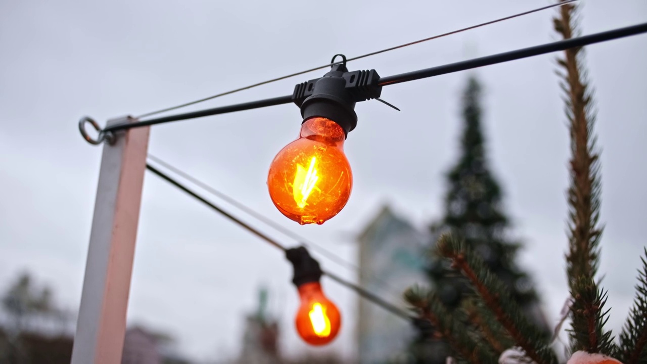 钨丝白炽灯装饰灯泡与温暖的橙色挂在户外防水电源线视频素材