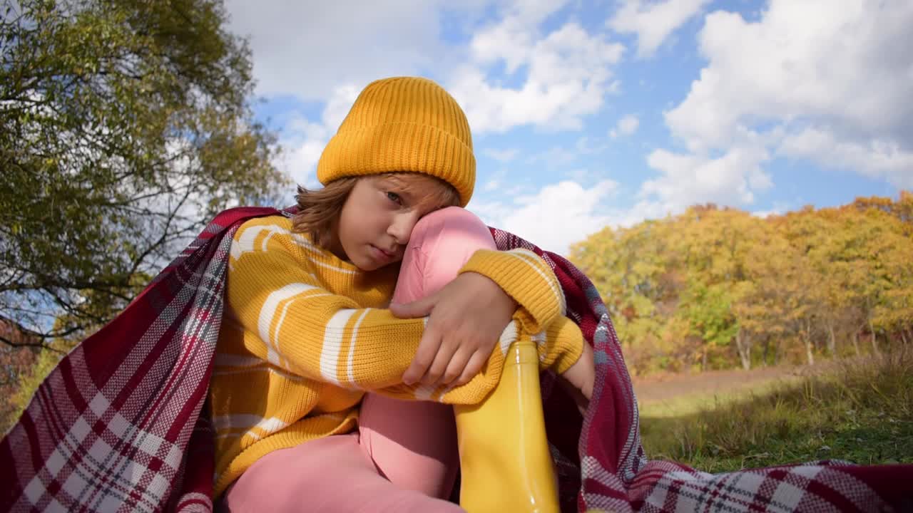 近距离的徒步旅行女孩坐在一块空地上，穿着胶靴和夹克，环顾四周。在阳光明媚的秋天，在森林里放松。慢动作视频。视频素材