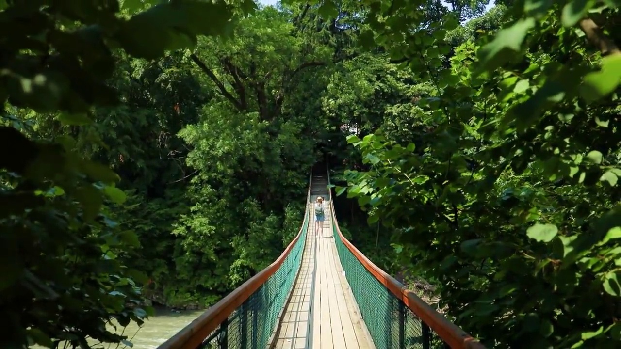 背包女徒步旅行者走在桥上过河。年轻的女子旅行者看着美丽的风景视频素材