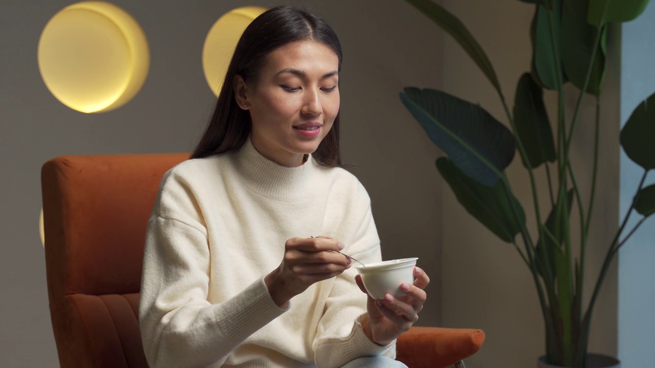 可爱的年轻女人坐在家里的椅子上吃酸奶视频素材