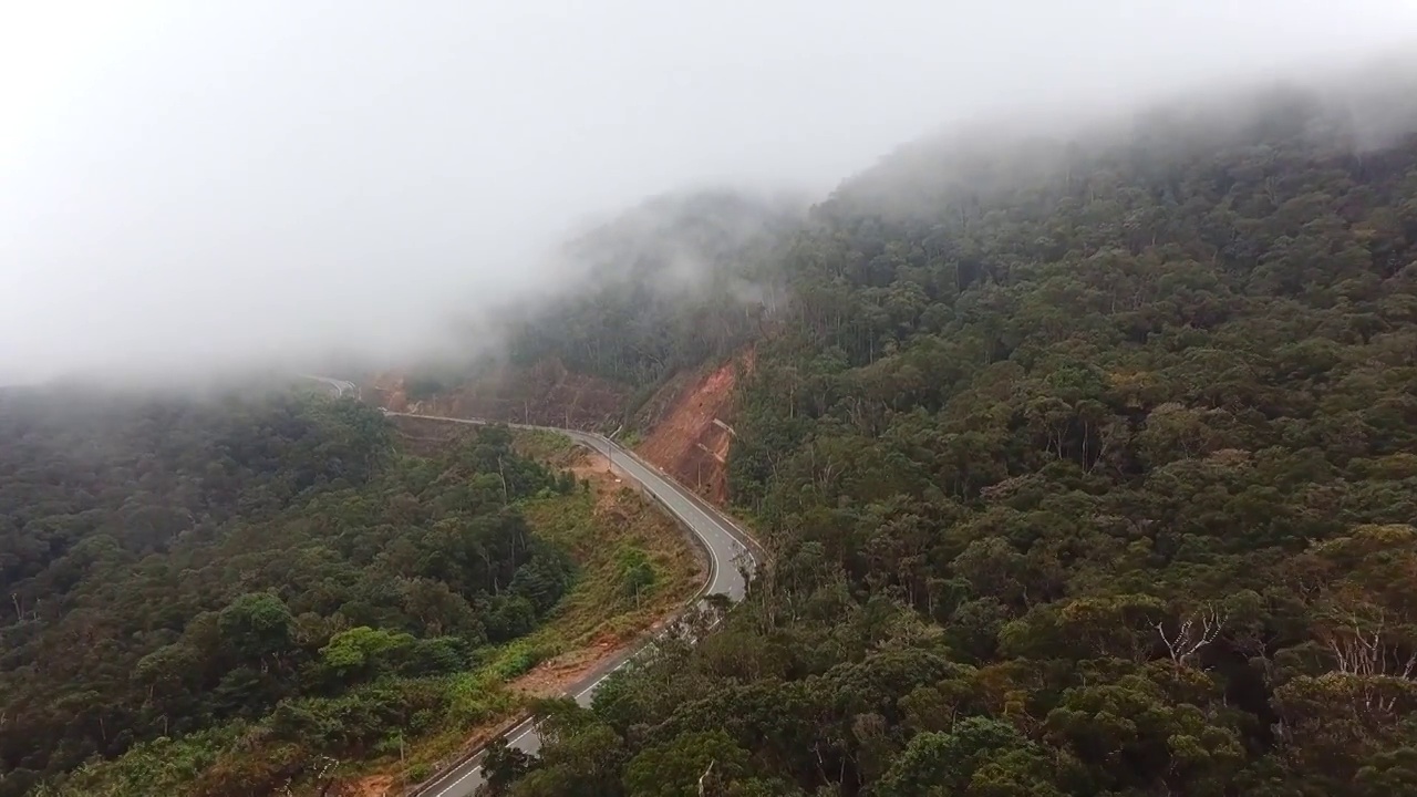 无人机在雾缭绕的山路上飞行，附近是雾蒙蒙的热带雨林。电影镜头航拍壮丽的热带山脉景观。视频素材