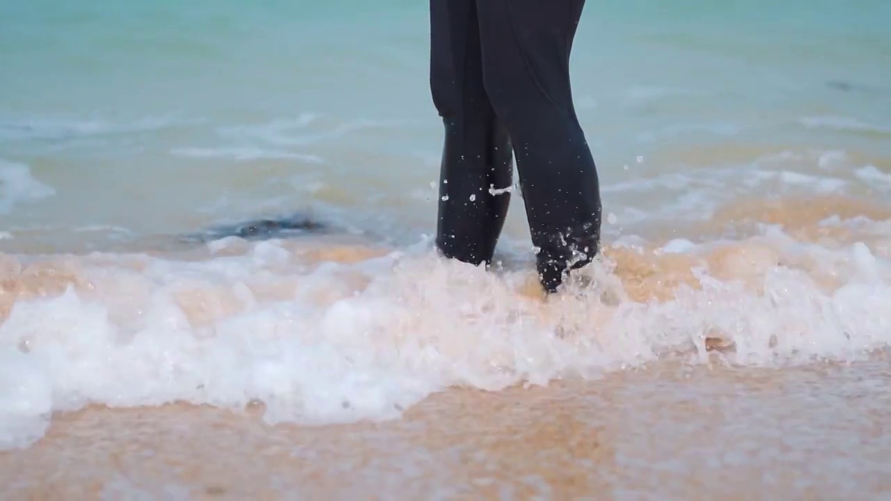 近距离拍摄的年轻女子赤脚站在海滩上。浪涛触足。夏季的热带海滩背景。旅游和假期的概念视频素材