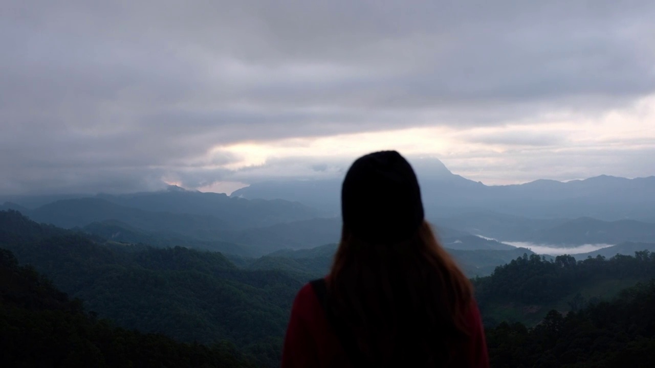 一个女性旅行者的后视图，看着一个美丽的山景在雾天视频素材