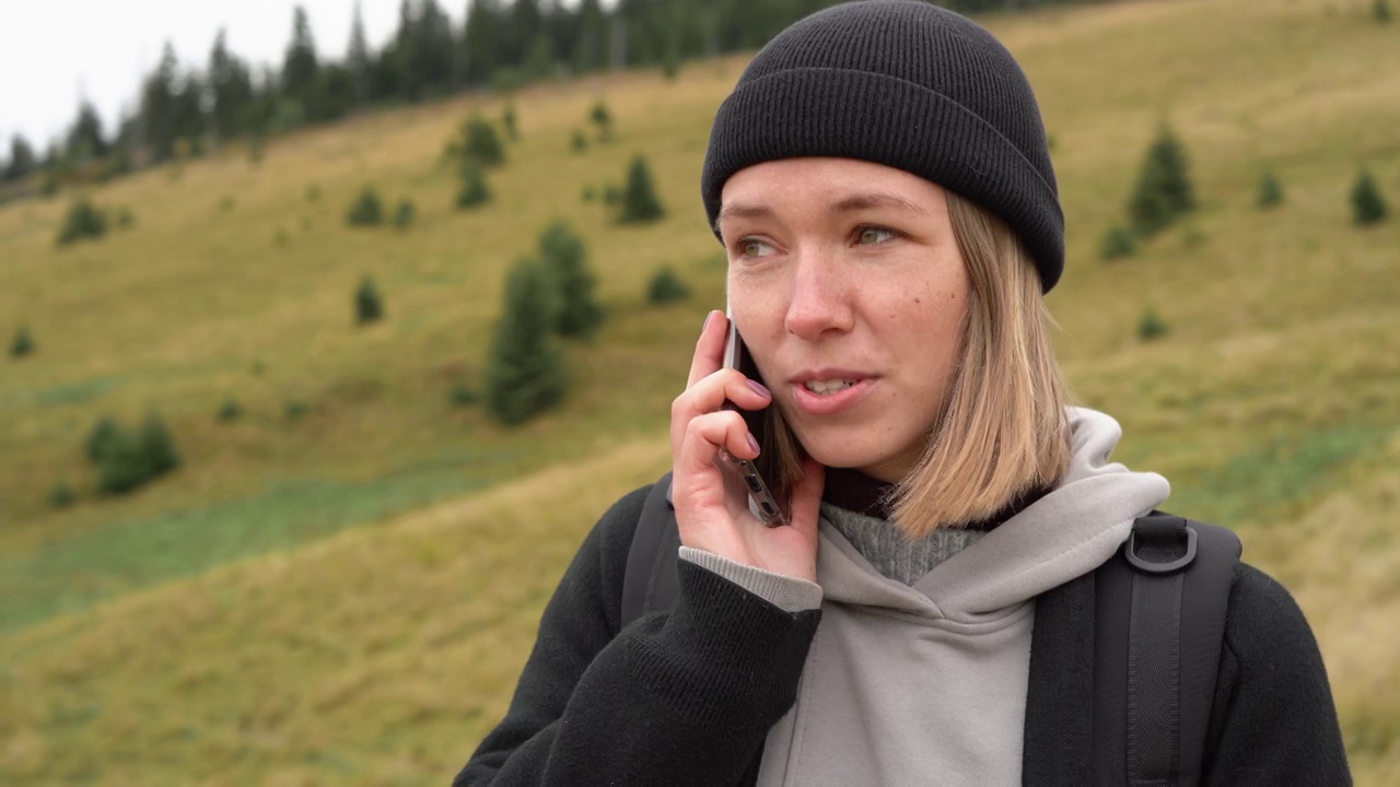 利用通讯技术的徒步旅行概念。白种人女人金发在山上徒步旅行时打电话给她的手机。视频素材