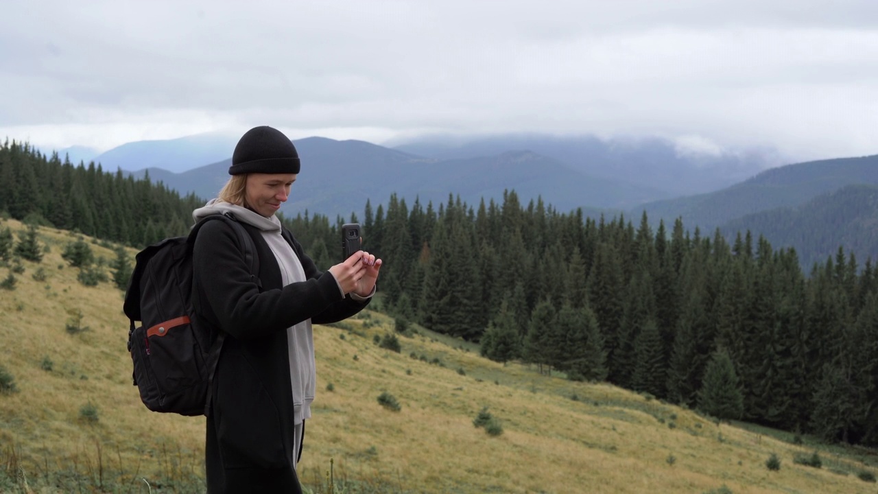 女人在长满草的山上旅行。山地景观中有雾和多云天气。用智能手机拍照的女孩。视频素材