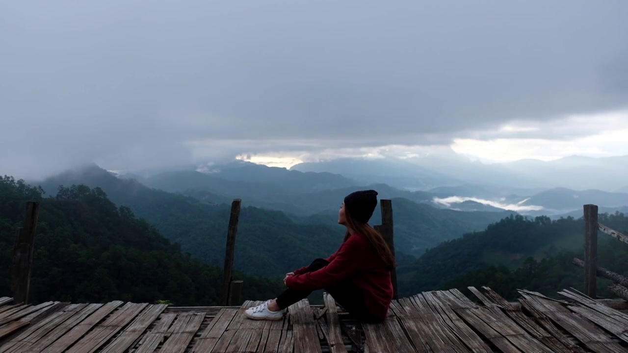 慢动作的一个女性旅行者坐在和看着美丽的山景在雾天视频素材