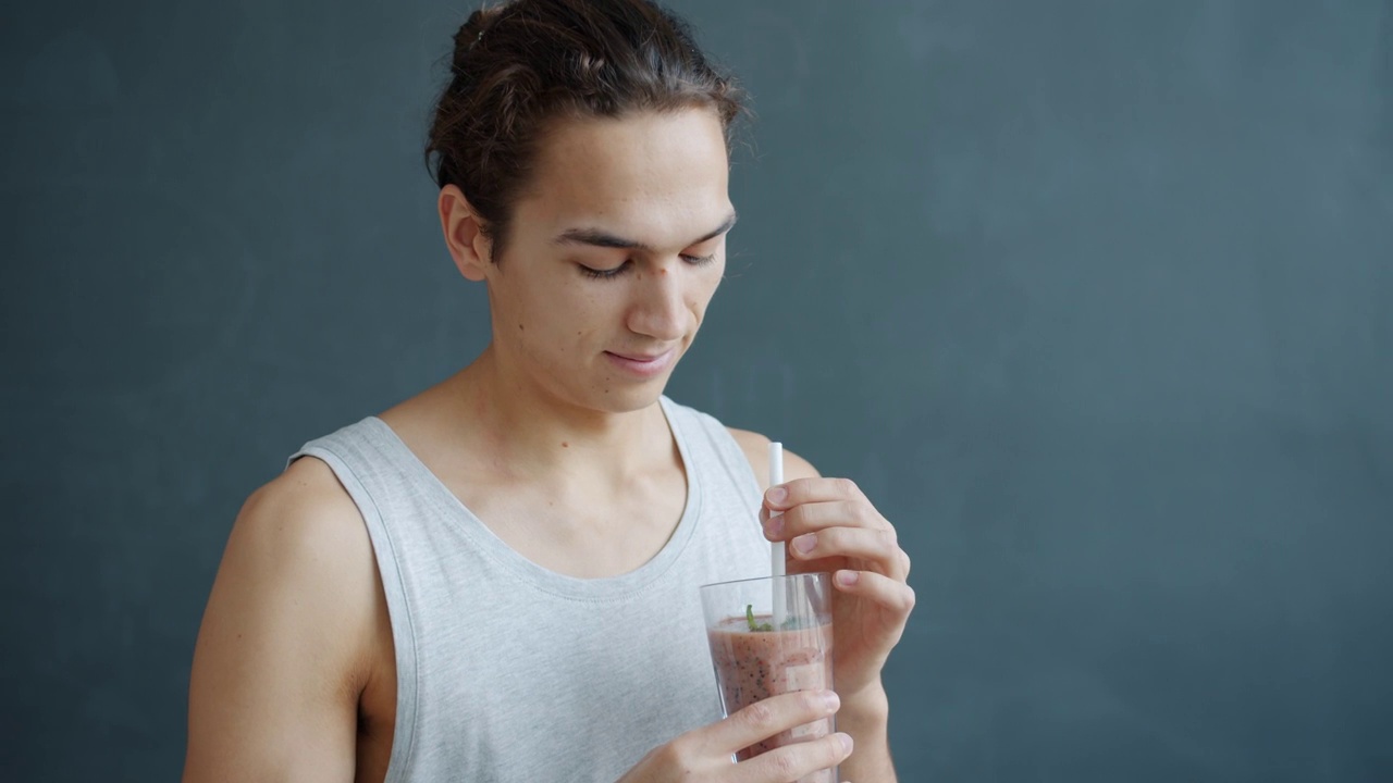 吸引人的年轻混合种族男子的肖像，拿着一杯清爽的冰沙，看着相机视频素材