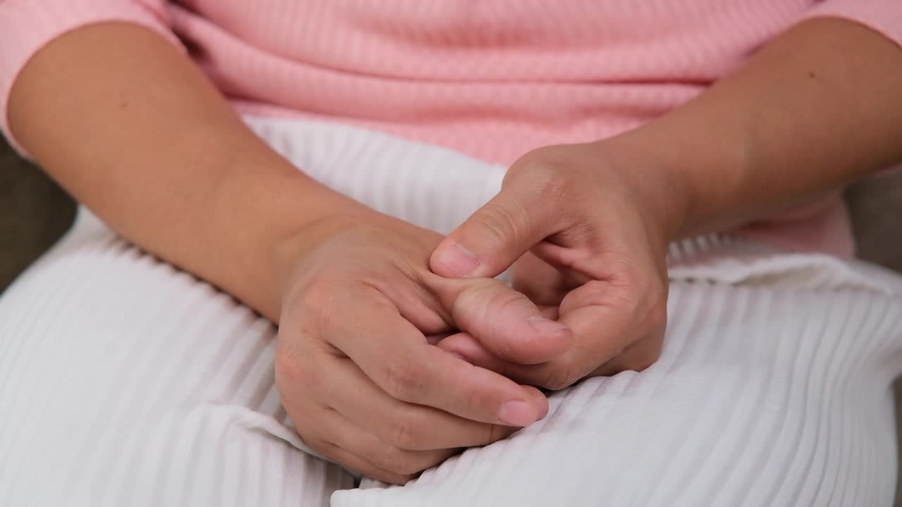 年轻女子坐在沙发上感觉手腕疼痛，她在家按摩手腕。腕关节损伤或慢性关节炎炎症。医疗保健和医疗概念。视频素材