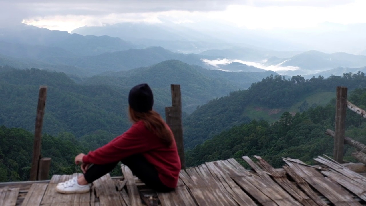 慢动作的一个女性旅行者坐在和看着美丽的山景在雾天视频素材