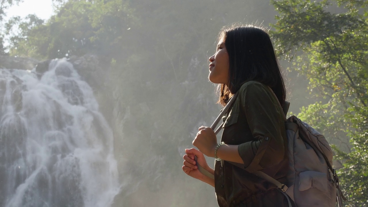 背着背包的旅行女人站在热带雨林和大瀑布的观点。视频素材