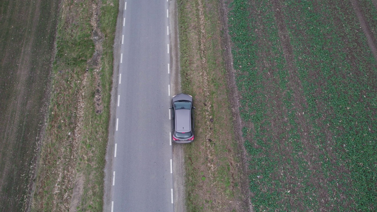 汽车正行驶在穿过田野的道路上，无人机拍下了鸟瞰图。秋天的时候在柏油路上，镜头跟着车走。视频素材