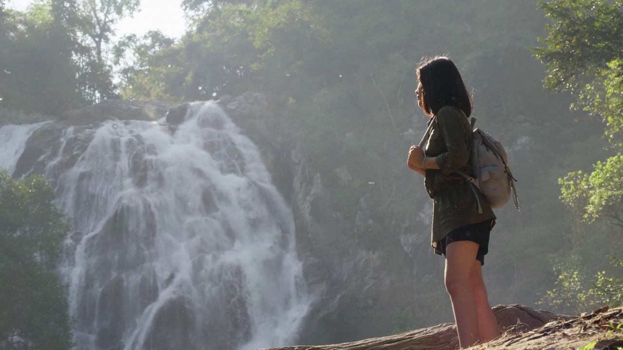 背着背包的旅行女人站在热带雨林和大瀑布的观点。视频素材