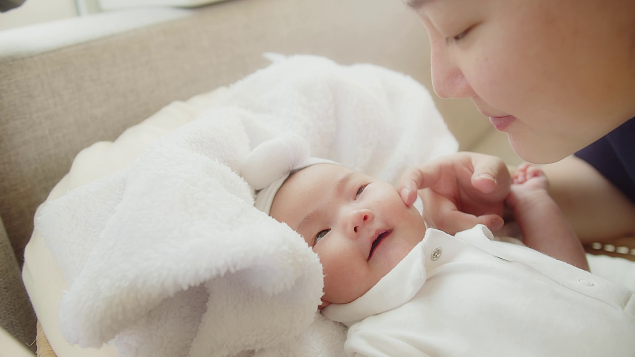 幸福家庭年轻的亚洲母亲抱着她漂亮的新生婴儿在家里的床上亲吻着婴儿，孩子，父母，童年，生活，母性，母爱的概念视频素材