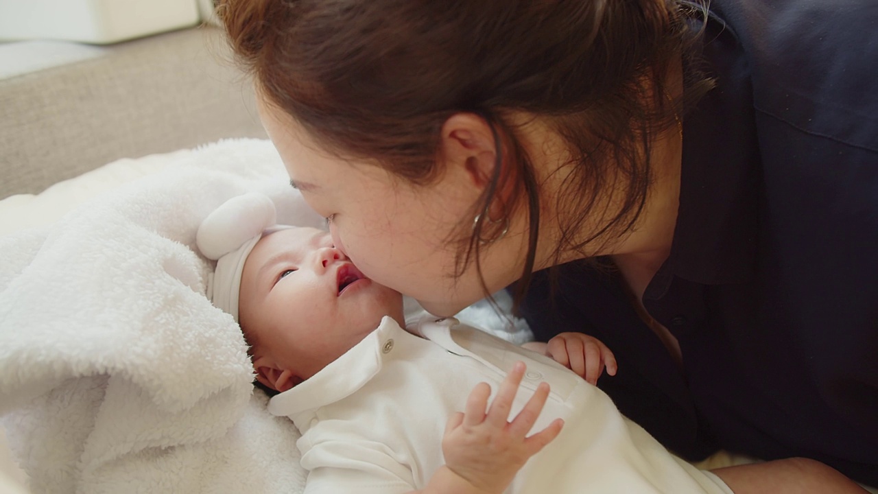 幸福家庭年轻的亚洲母亲抱着她漂亮的新生婴儿在家里的床上亲吻着婴儿，孩子，父母，童年，生活，母性，母爱的概念视频素材