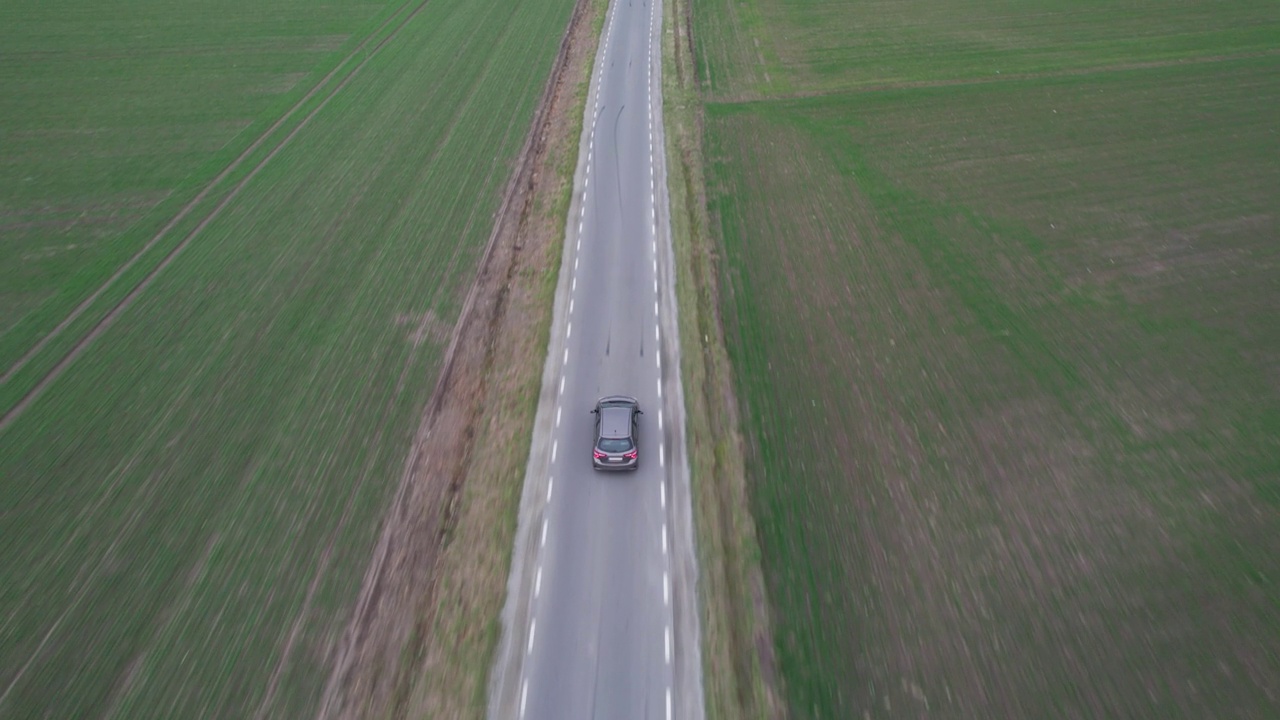 汽车正行驶在穿过田野的道路上，无人机拍下了鸟瞰图。秋天的时候在柏油路上，镜头跟着车走。视频素材