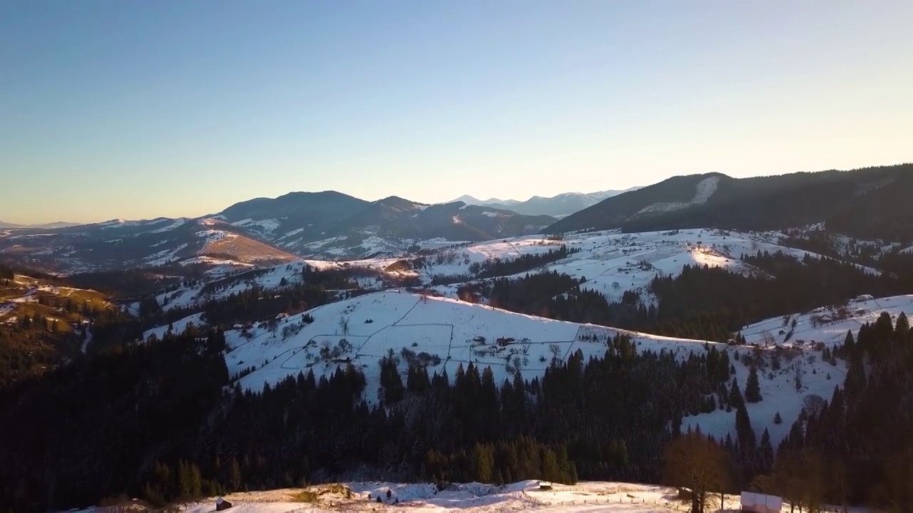 鸟瞰乌克兰喀尔巴阡山脉，冬天白雪覆盖的山坡上散落着房屋。视频素材