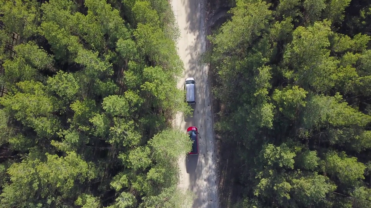 两辆红色和银色的小型货车正沿着森林道路行驶。从以上观点。从无人机上拍摄时，摄像机移到左边视频素材