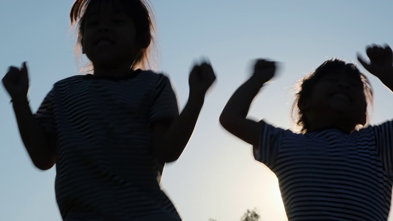 夕阳西下的夏日花园中，快乐的姐妹们举手跳跃的剪影。欢快的女孩在公园里蹦蹦跳跳。视频素材