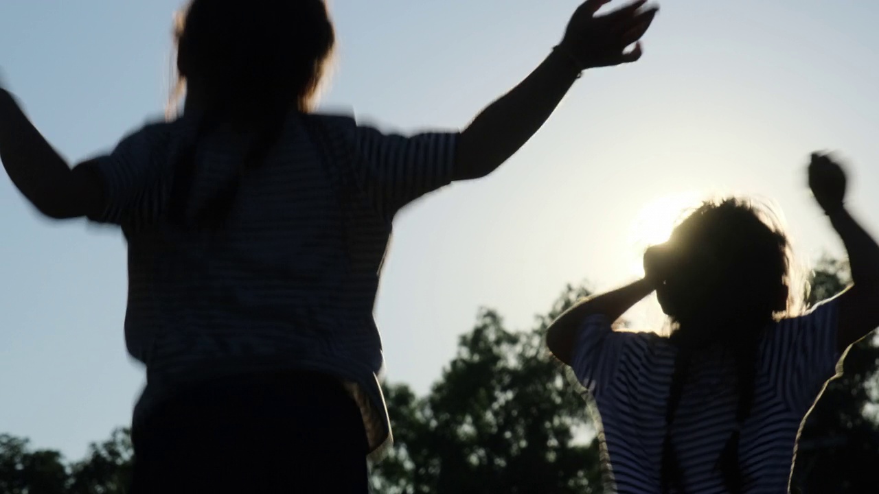 夕阳西下的夏日花园中，快乐的姐妹们举手跳跃的剪影。欢快的女孩在公园里蹦蹦跳跳。视频素材