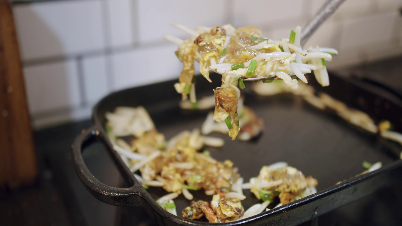 近距离烹饪泰国街头小吃酥脆炸贻贝煎饼，鸡蛋芽和小葱在厨房的热铁锅上视频素材