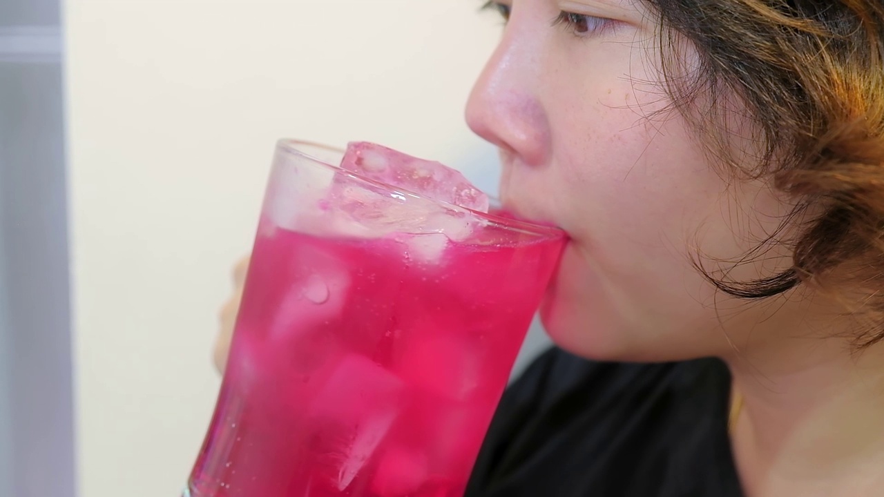 年轻的亚洲女子喝着红色苏打水用杯子里的冰块浓缩调味糖浆，夏日里的饮料甜而爽口视频素材