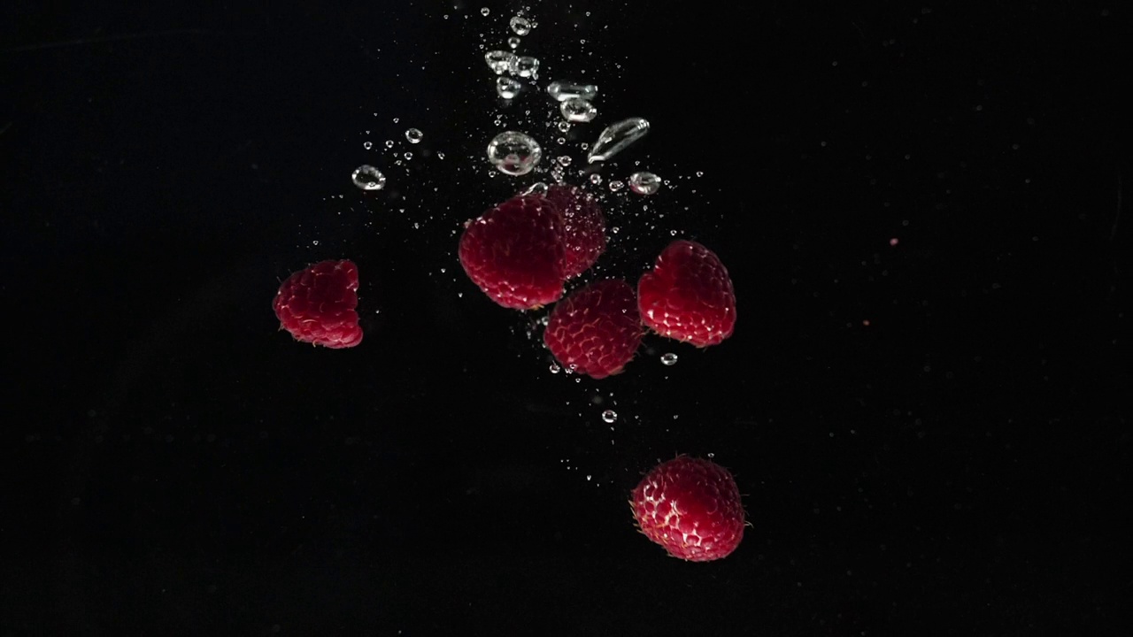 新鲜健康的食物。红色的覆盆子掉进黑色背景的水中。新鲜的水果在水族馆里飞溅。有机浆果，清洁饮食，节食，排毒，素食，纯素食品的概念。慢动作视频素材