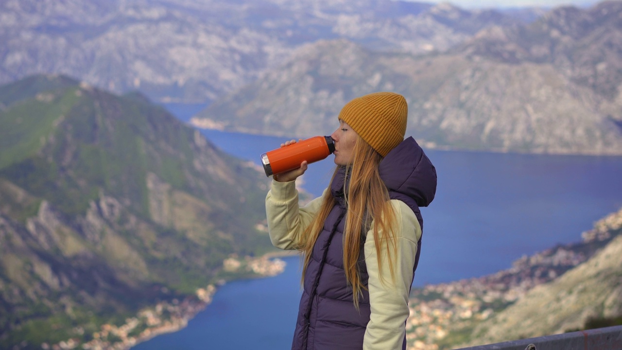 秋天，一名女子在黑山旅行。她喝着保温瓶里的热饮，背景是波卡科托斯卡湾视频素材