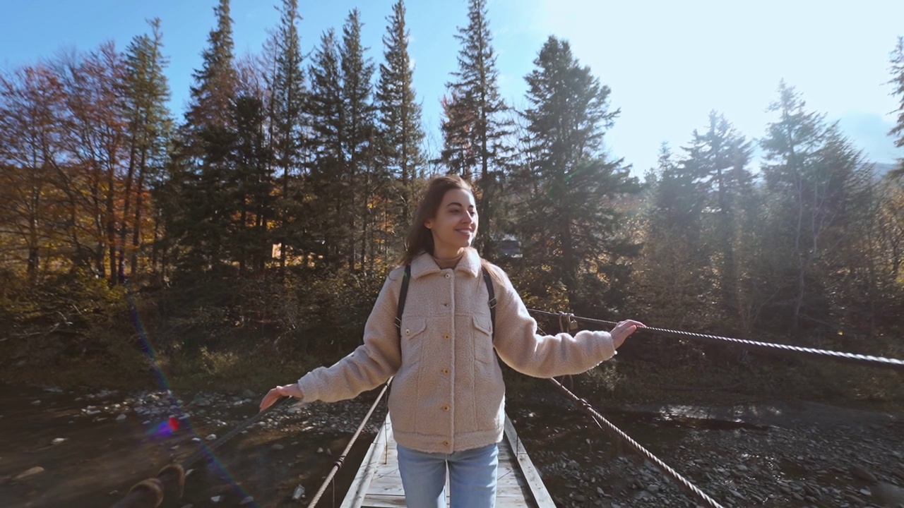 快乐美丽的年轻女子游客站在悬索桥悬山河的慢动作肖像。令人惊叹的景观云杉，山脉和天空的背景视频素材