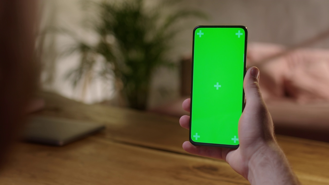 手持相机:年轻人在家里手持色度键绿色屏幕智能手机观看内容，无需触摸或滑动。浏览互联网，观看内容，视频视频素材