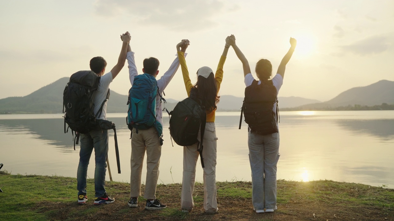 四名亚洲成年男女携带旅行包，旅行到终点，享受你的一天，放松你的手。在日落。它有水库视图和背景山。视频素材