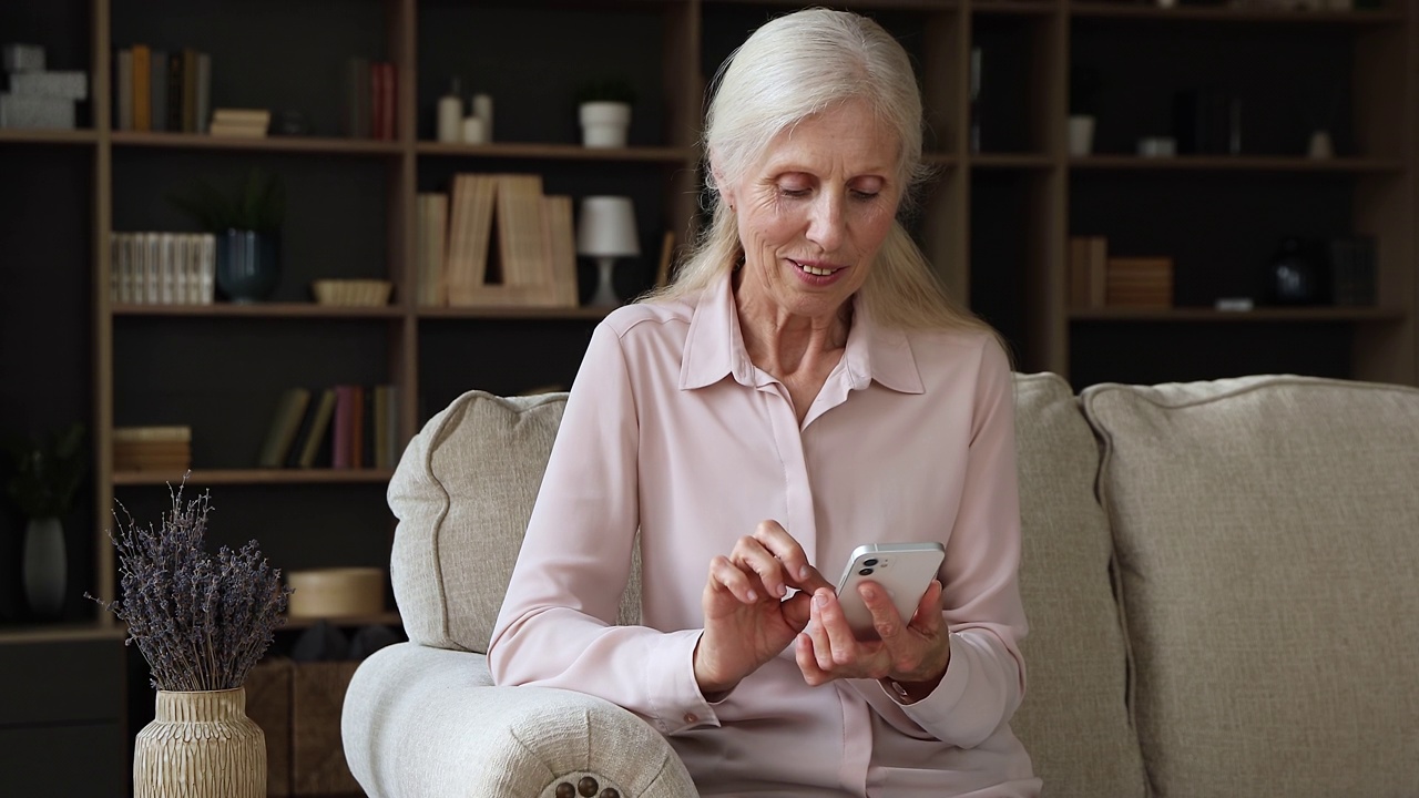 有魅力的老女人坐在家里的沙发上用智能手机视频素材