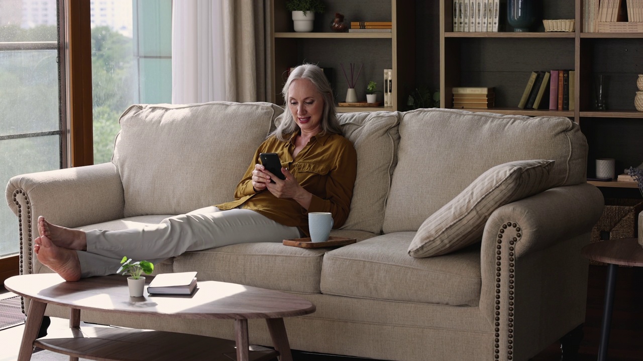漂亮的老年女性坐在沙发上用手机视频素材