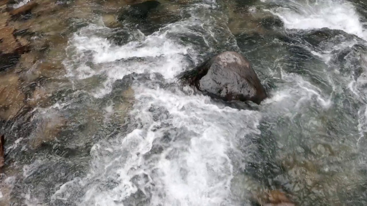 在山涧中，溪水湍急地流过，蓝色的水和白色的泡沫围绕着许多鹅卵石视频素材