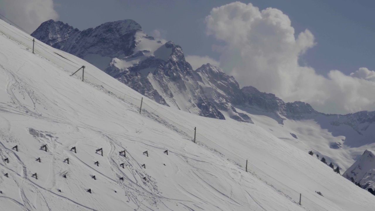 在大雪覆盖的陡峭山坡上，通过巨大的金属杆攀爬的缆车视频素材