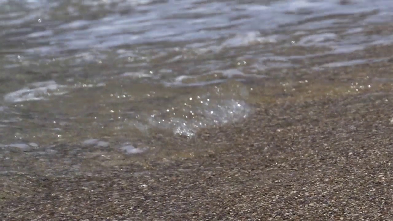 海浪从粗糙的沙子中劈开，形成泡沫视频素材