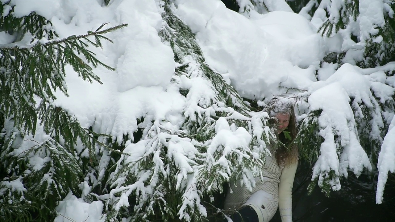 雪落在一个美丽的女人身上。一个成年白人女孩在冬天的森林里散步。在松树公园散步。冬天玩得开心，享受户外散步。视频素材