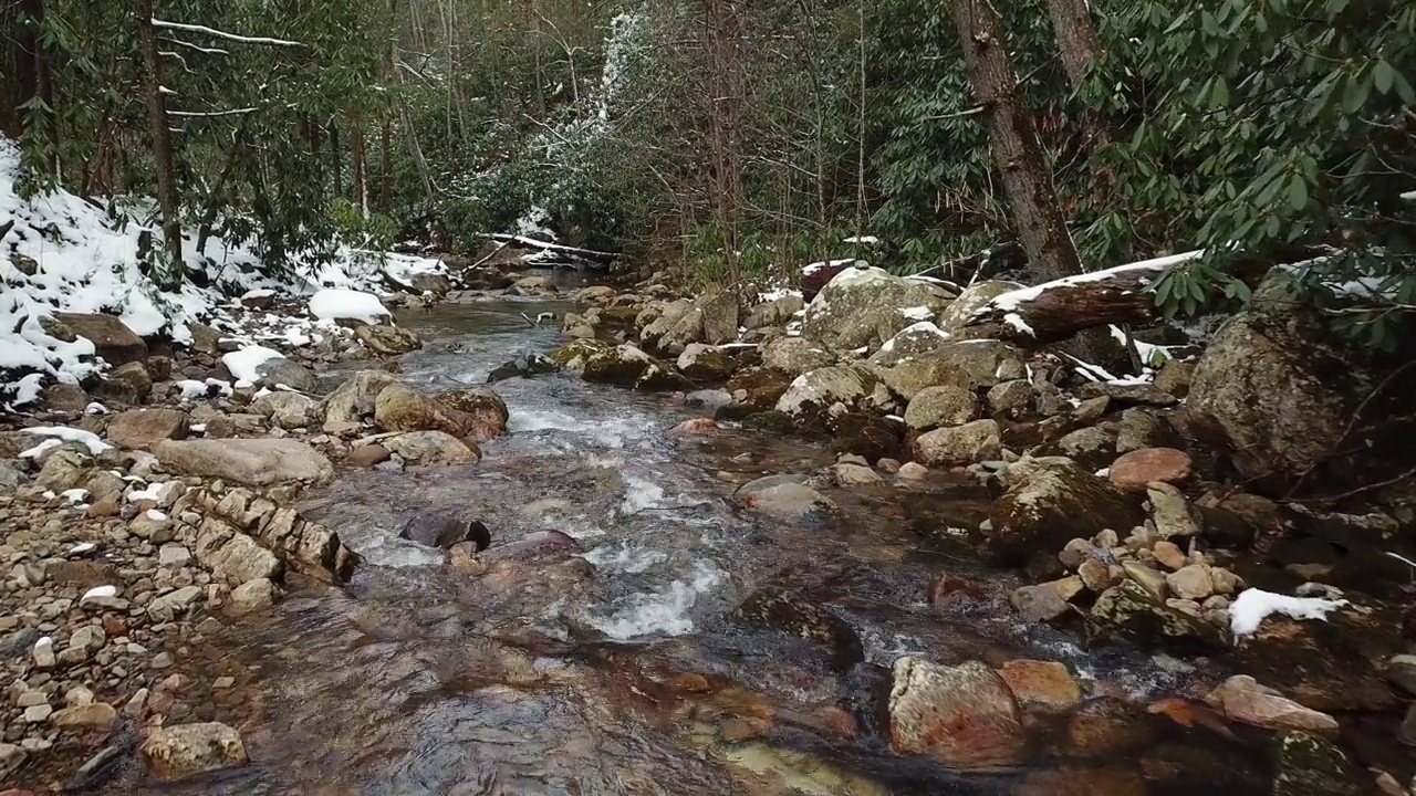 低空飞行的无人机在冬季雪中流动的岩石溪流的视图视频素材