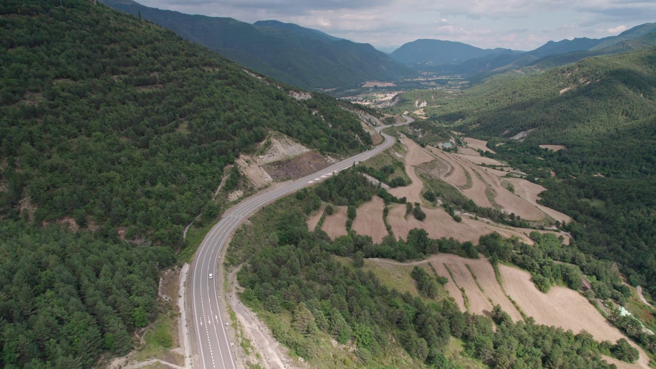 美丽的无人机视图沥青道路在高山上。山脉消失在天空中，天空略有多云，但山峰被太阳照亮。视频素材