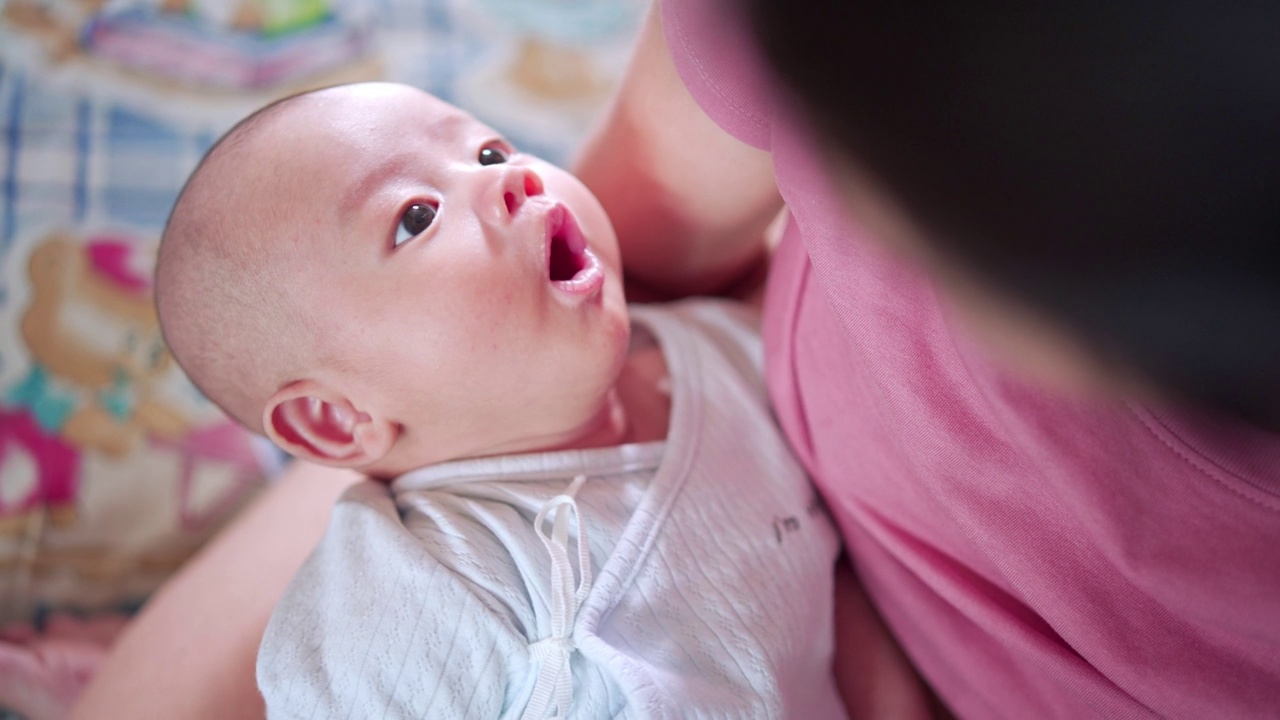 可爱的亚洲新生儿快乐，母亲母乳喂养和拥抱婴儿。宝宝醒来后吃着牛奶，脸上带着幸福的笑容，开心地看着妈妈。哺乳婴儿的概念。关键词:婴儿母乳喂养视频素材