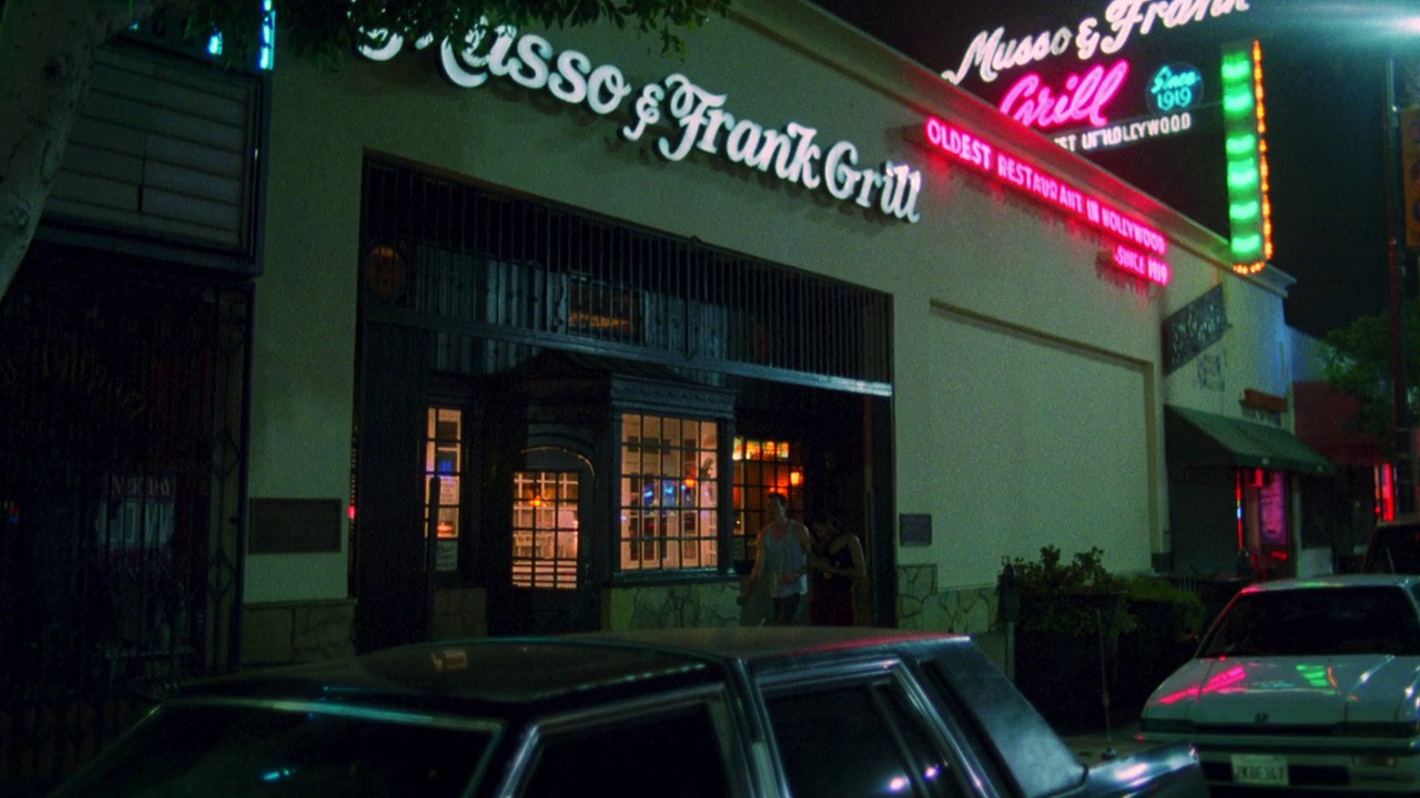 中角的“musso & frank grill”餐厅招牌。餐厅入口上方的“musso & frank grill”霓虹灯招牌。人们走在人行道上。停着的汽车。好莱坞的大街。视频素材